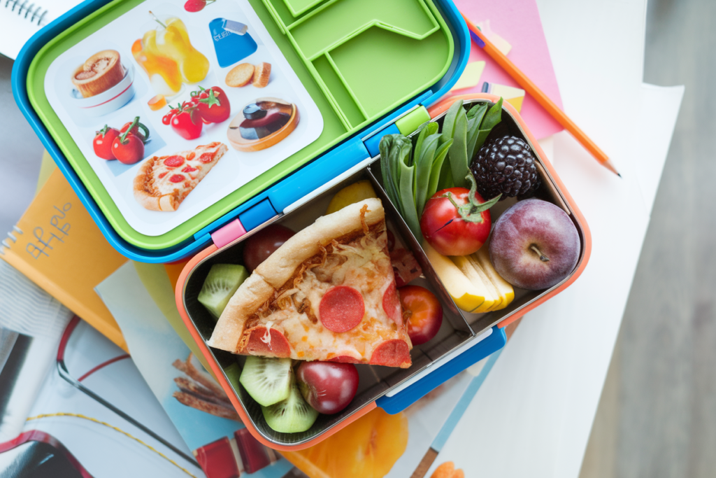 Overhead view of a packed lunchbox with pizza, vegetables, and fruit for school lunch